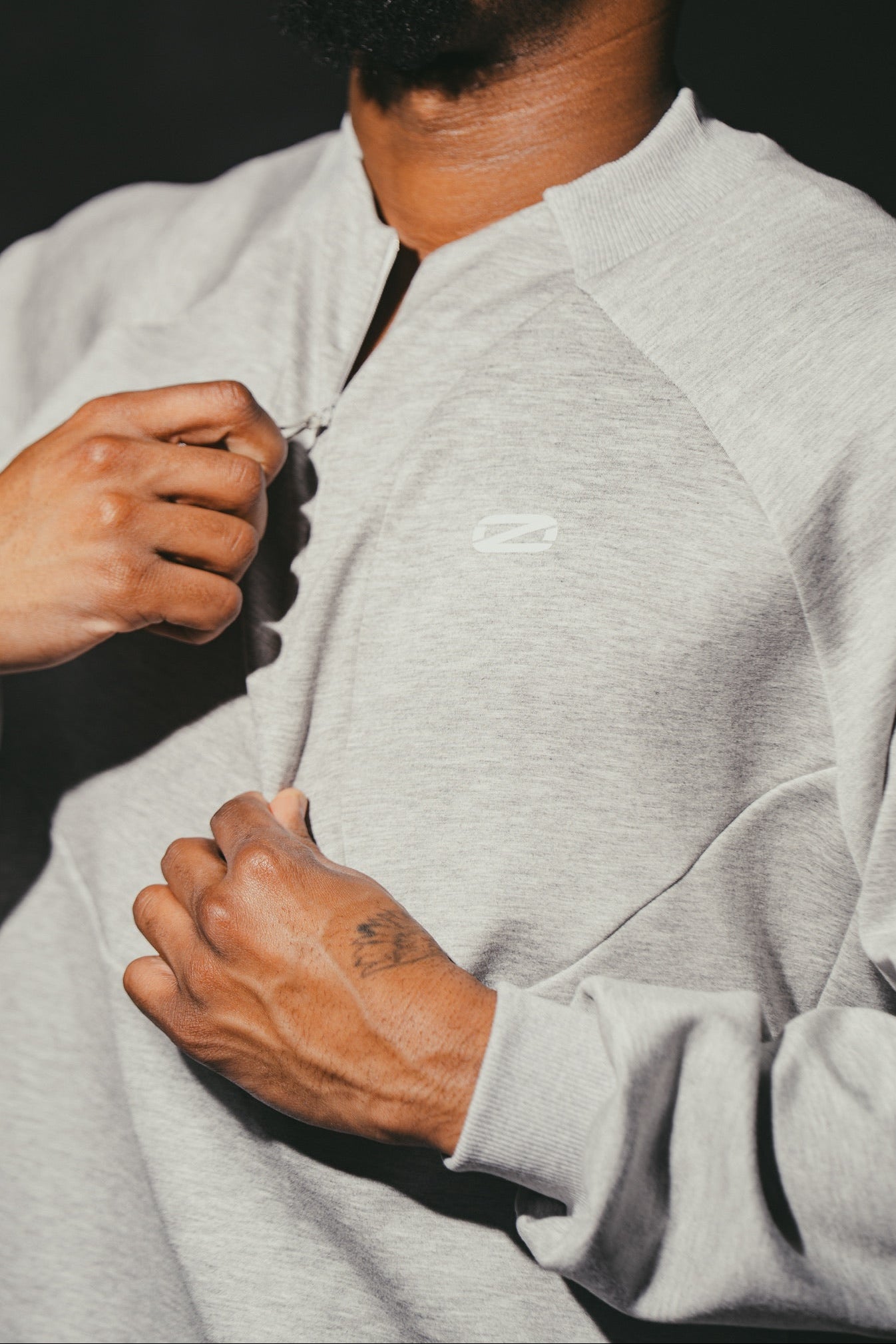 Man wearing a gray sweatshirt with a brand logo, against a dark background